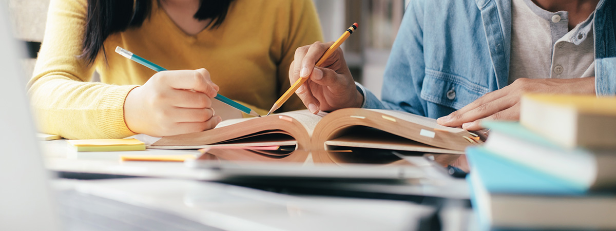 close up of books and people holding pencils